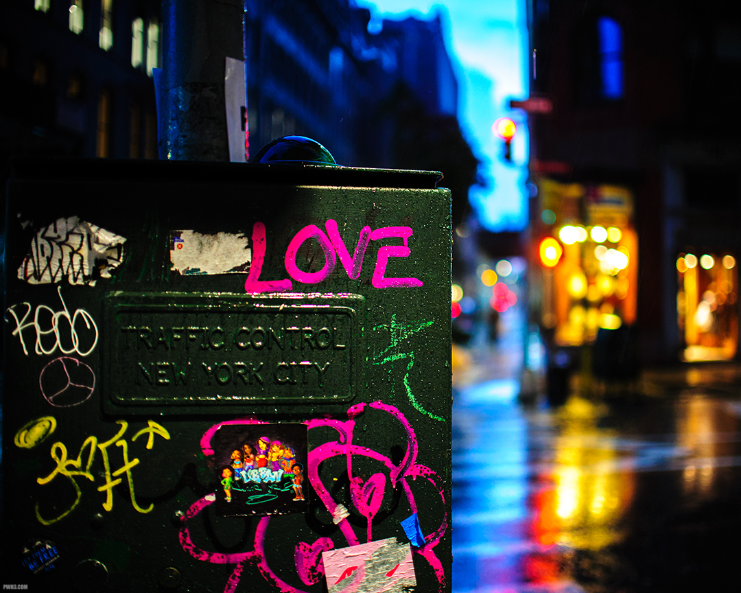 Graffiti on a traffic control box in the rain at night in NYC.