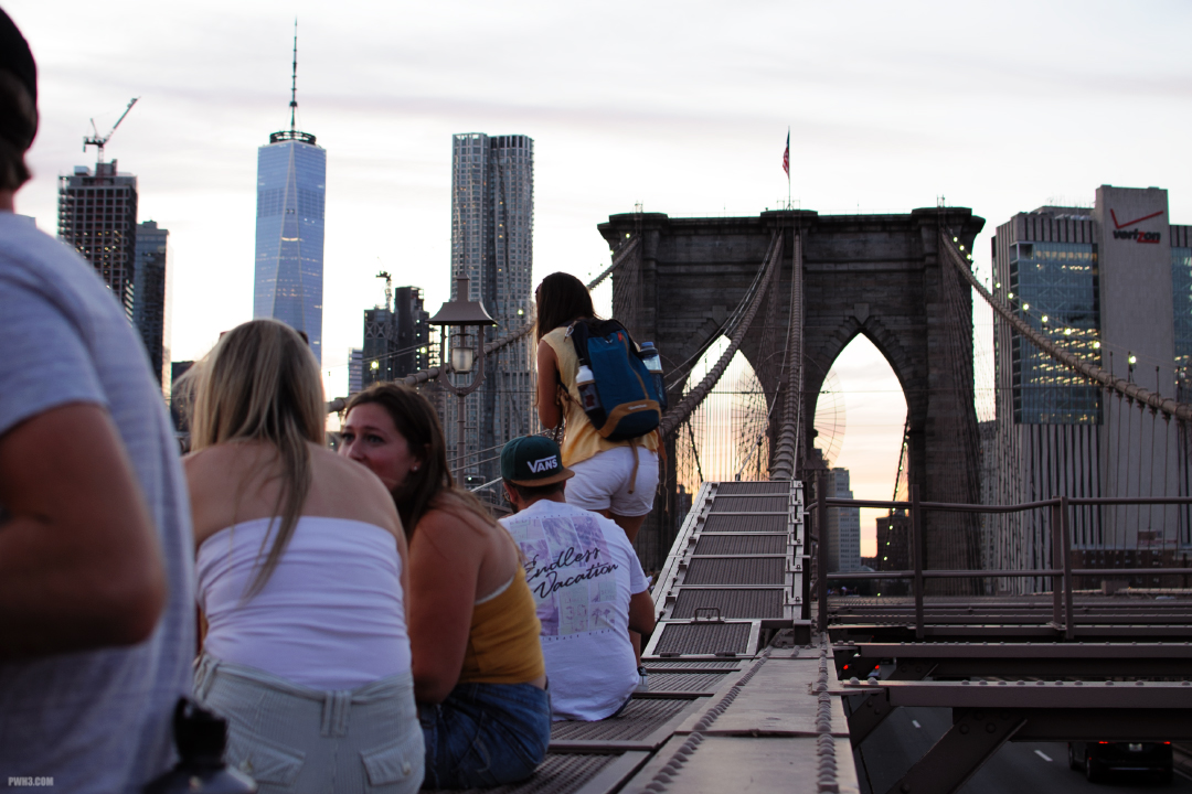 Young people sitting and talking on the girders of the Brooklyn Bridge.