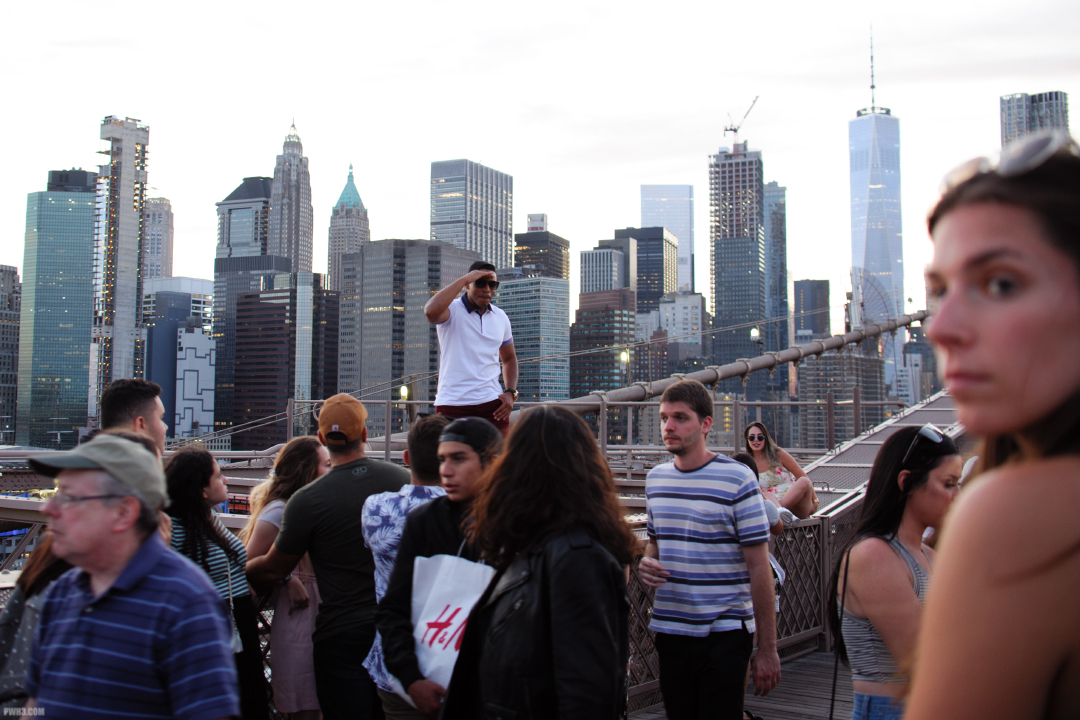 A young man salutes while standing on a girder of the Brooklyn Bridge.