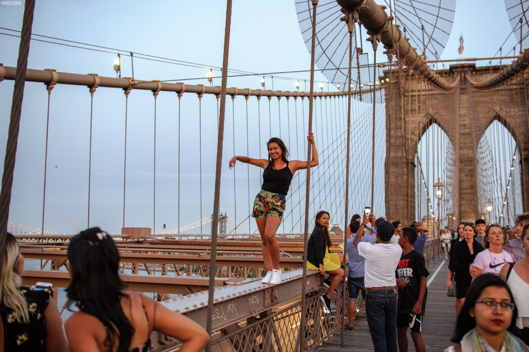 A young woman has climbed onto a girder to strike a pose on the Brooklyn Bridge.