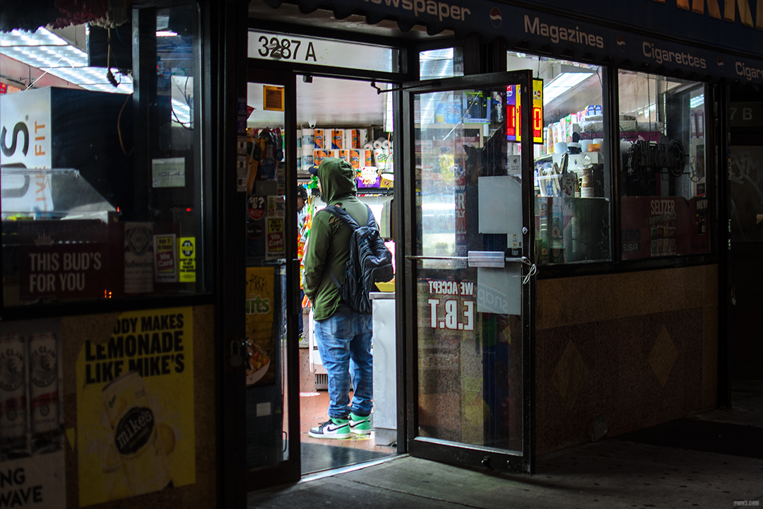 Man in the doorway of a deli, wearing a green hoodie.